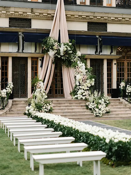 Blush Fabric Arch, White Ivy Aisle Flowers, Stone Staircase Behind the Arch, and White Bench
