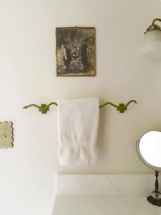 Vintage European apartment style wall arrangement with a green painted curved towel bar holding one white hand towel below a small black-and-white photo in a brass frame