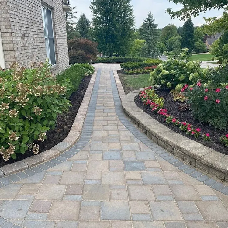 Curved Stone Paver Walkway in Tan Gray and Beige by a Raised Flower Bed and Low Stacked Stone Wall on One Side