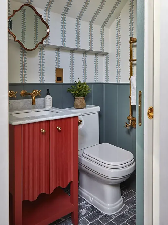 Blue-Gray Lower-Wall Paneling below Geometric Wallpaper and a Red Vanity with Gold Knobs