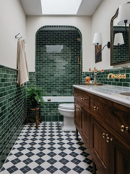 Dark wood antique vanity with a brass vanity fixture and dark green subway tile on the lower walls and alcove