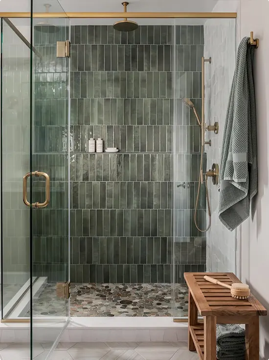 Muted slate green vertical tile stack, brass hardware, pebble floor