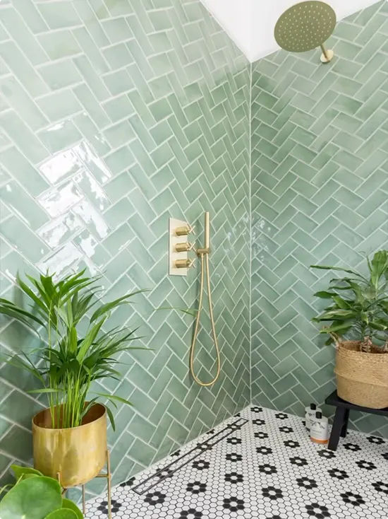 Soft sage green metro tile in a herringbone pattern with a gold fixture, two plants and black and white hexagon floor tile