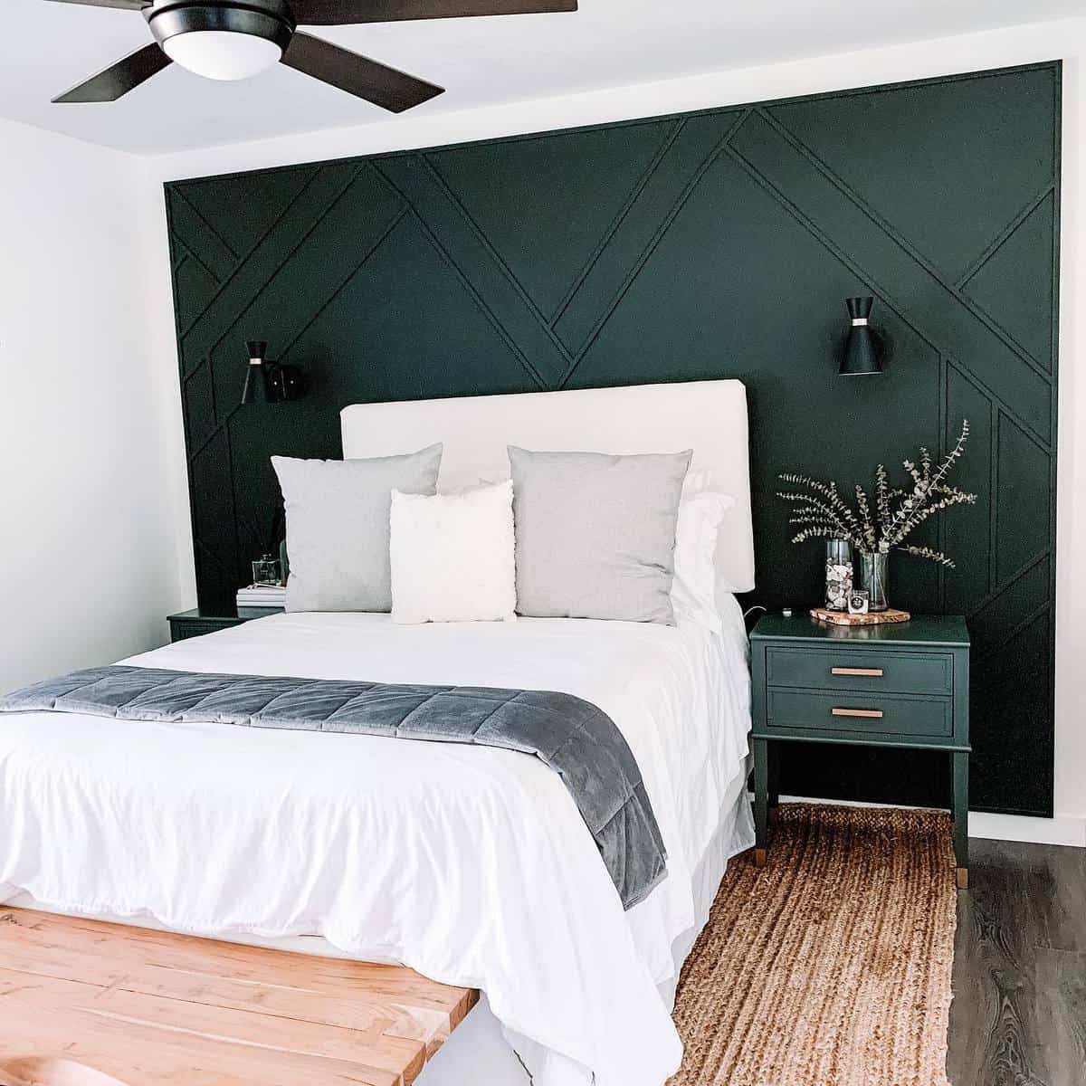 accent-wall-green-bedroom-ideas-elementsofmoving Modern bedroom with dark green accent wall, white bedding, gray pillows, bedside tables, and a ceiling fan
