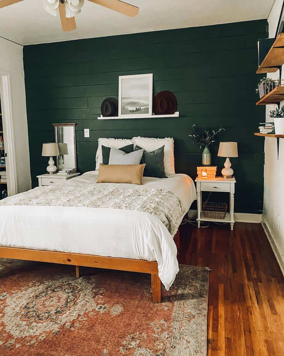 accent-wall-green-bedroom-ideas-uniquelytaylormade Cozy bedroom with a green accent wall, white bed, wooden floor, lamps on nightstands, and decorative pillows