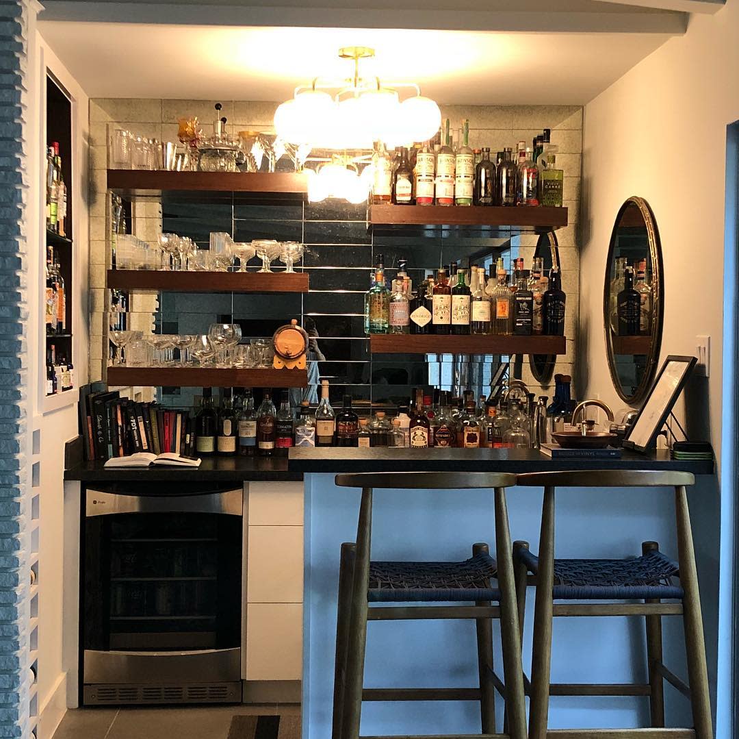 bars20basement20apartment20ideas20-mommymixology Fully stocked home bar with wooden shelves, glassware, liquor bottles, and a small fridge.
