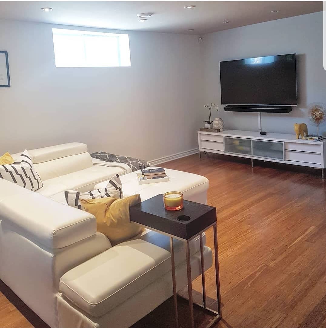 bathroom20basement20apartment20ideas20-designbyshieka Modern basement living room with white sectional, wall-mounted TV, and wooden floors.