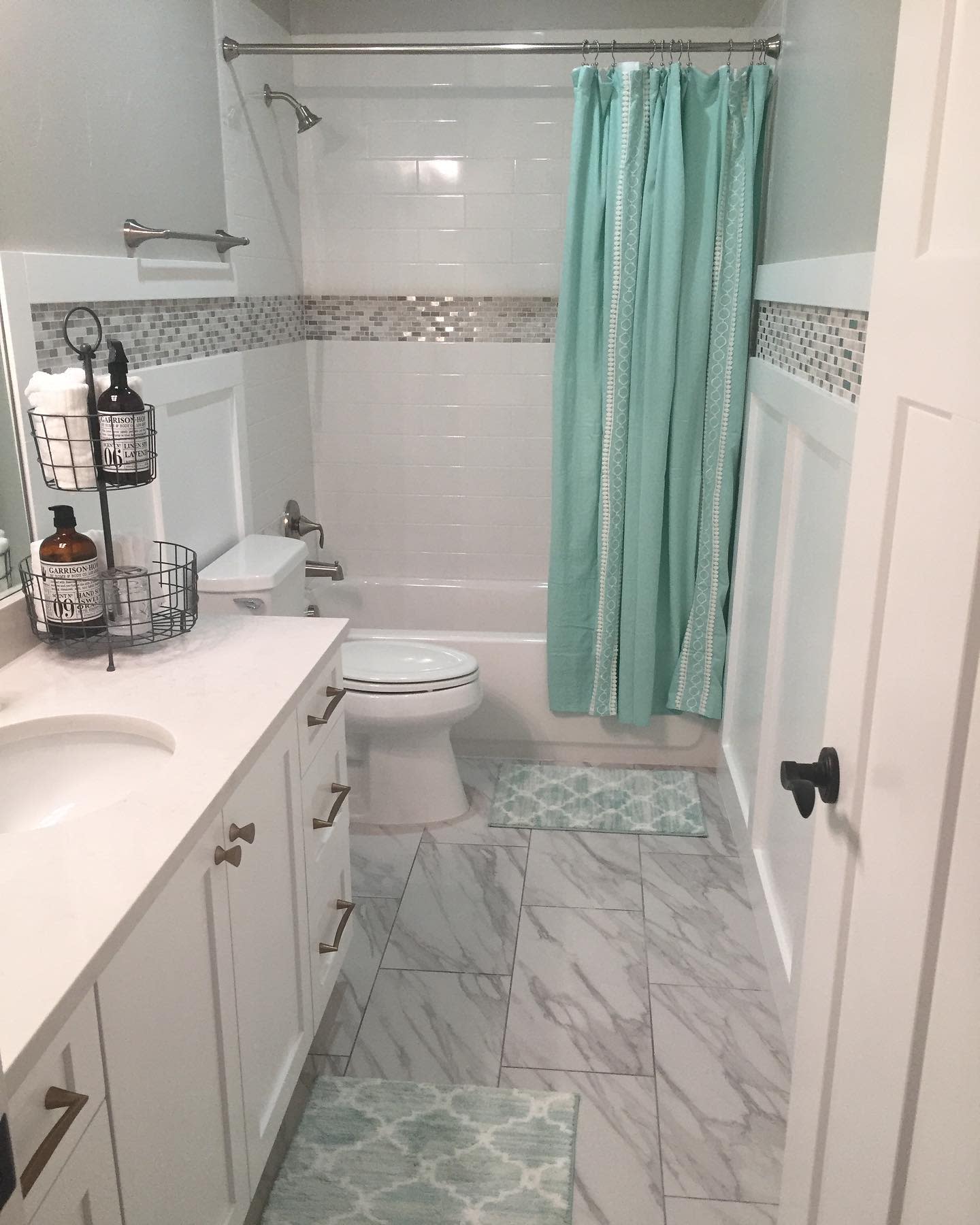 bathroom20basement20apartment20ideas20-jen_noble_home Bathroom with marble tile floor, white vanity, and aqua shower curtain.