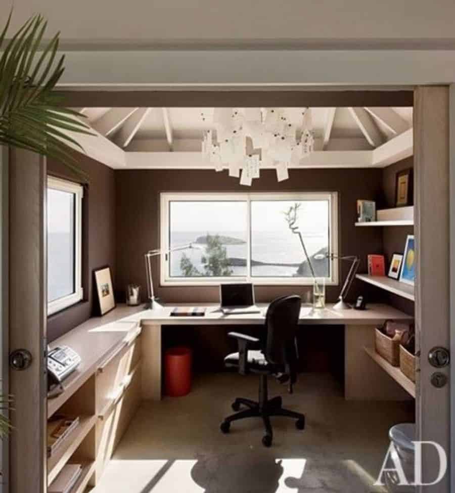 A cozy home office with a sea view, desk, chair, shelves, and a decorative ceiling light