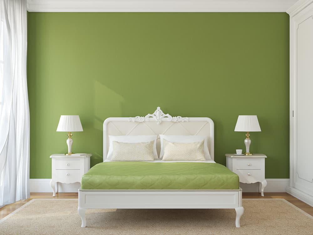 classic-green-bedroom-ideas-1 A bedroom with a green accent wall, white bed and furniture, and two lamps on nightstands