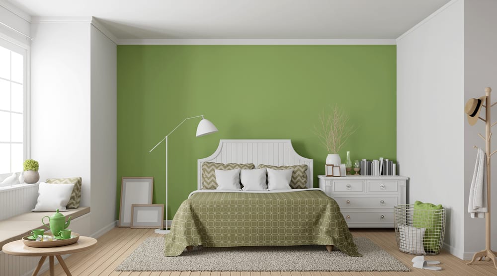 classic-green-bedroom-ideas-2 A cozy bedroom with a green accent wall, white bed, matching bedding, and a window seat. Decor is minimal and modern