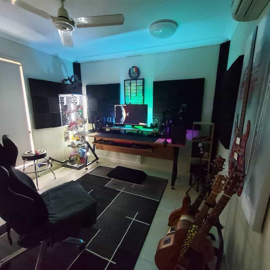 Gaming setup with a lit PC, monitors, acoustic panels, guitars, and a gaming chair in a modern room