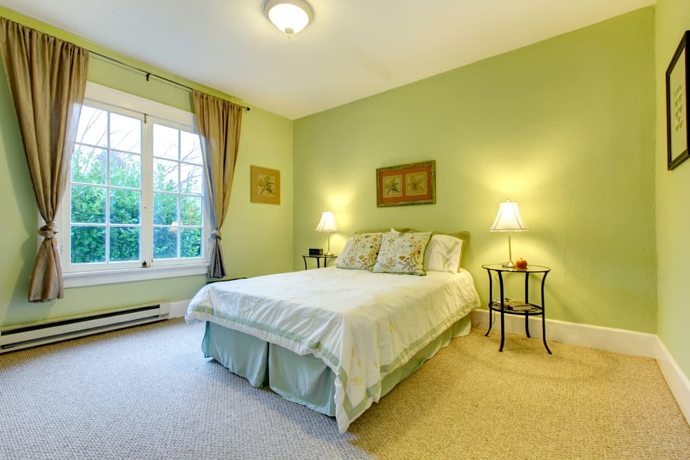 elegant-green-bedroom-ideas-1 Cozy bedroom with green walls, a double bed, and lamps on side tables next to a large window with curtains