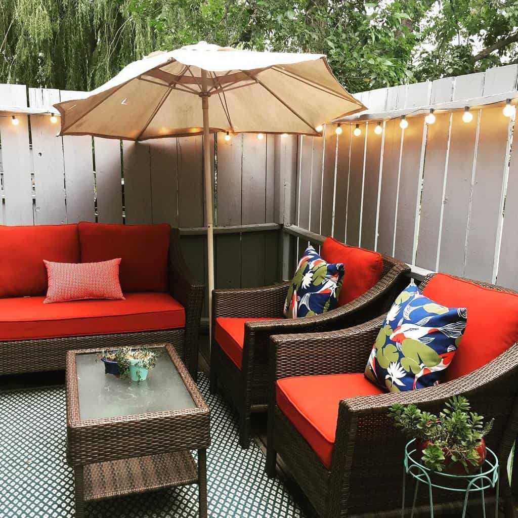 backyard corner white fence wicker furniture red cushions umbrella