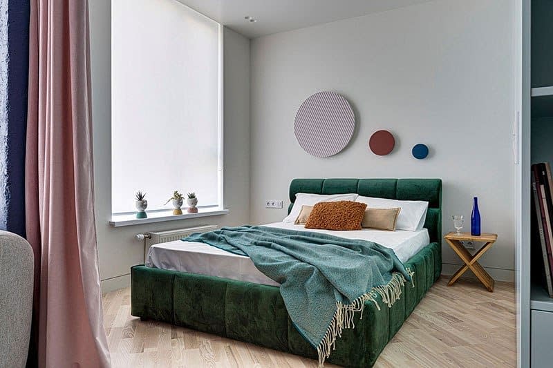 guestroom-green-bedroom-ideas-mbw_interiors Modern bedroom with a plush green bed, cozy pillows, and a teal throw featuring minimalist decor on light-colored walls