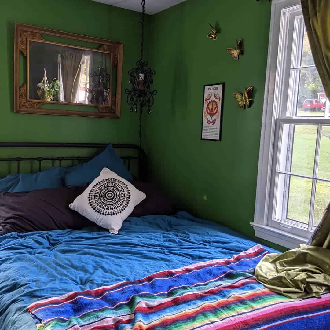 guestroom-green-bedroom-ideas-nashvillerealestatebroker Cozy bedroom with green walls, a bed with colorful blankets, decorative pillows, and a window with greenery outside