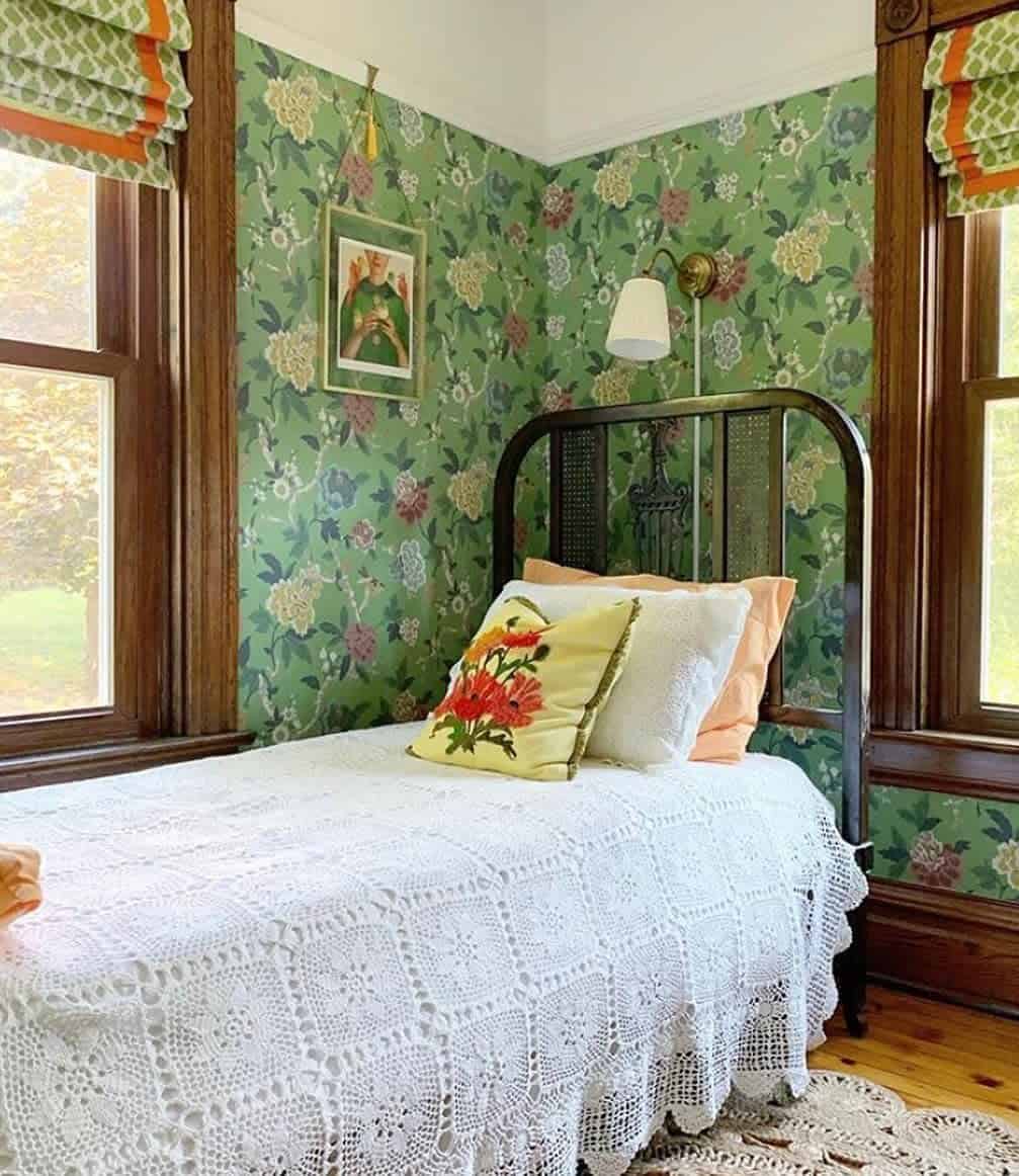 guestroom-green-bedroom-ideas-sewlovelybykelly Cozy room with floral wallpaper, vintage bed, crocheted blanket, and decorative pillow near two windows