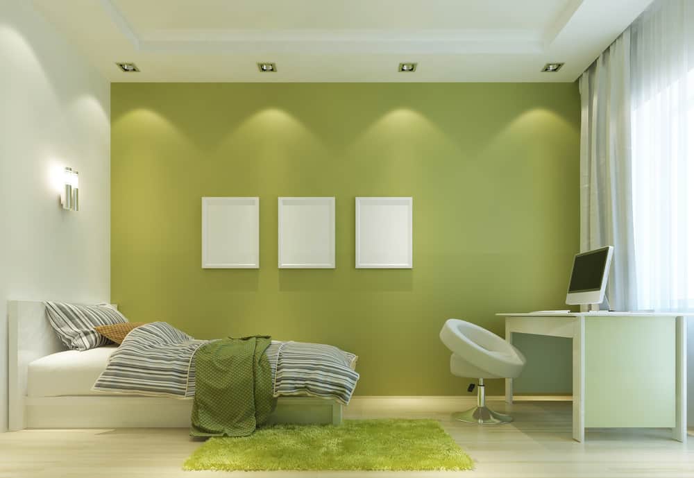 interior-green-bedroom-ideas-4 Minimalist bedroom with green accent wall, bed, desk, chair, and three white frames featuring natural light from window
