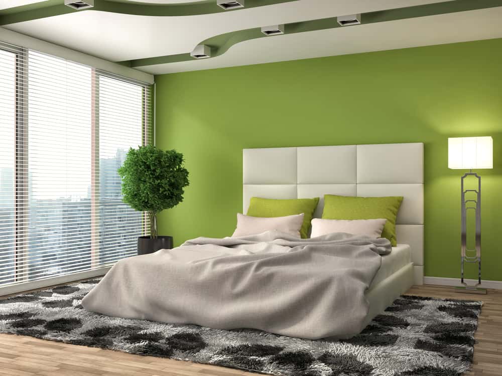 interior-green-bedroom-ideas-5 Modern bedroom with a green accent wall, white bed, green pillows, rug, tall plant, and floor lamp