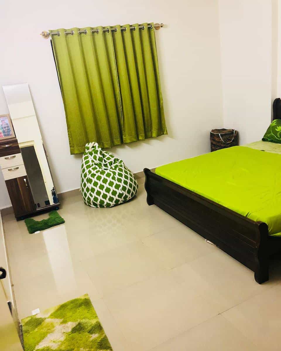 interior-green-bedroom-ideas-all_about_home_and_food Bedroom with green decor: bed, curtains, bean bag, and rug; white walls, a dresser, and a mirror are visible