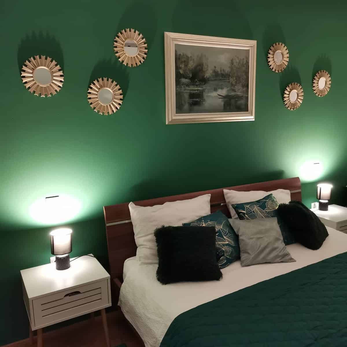 interior-green-bedroom-ideas-sviky15 Cozy bedroom with green walls, mirror decor, framed painting, and a bed with green quilt and cushions