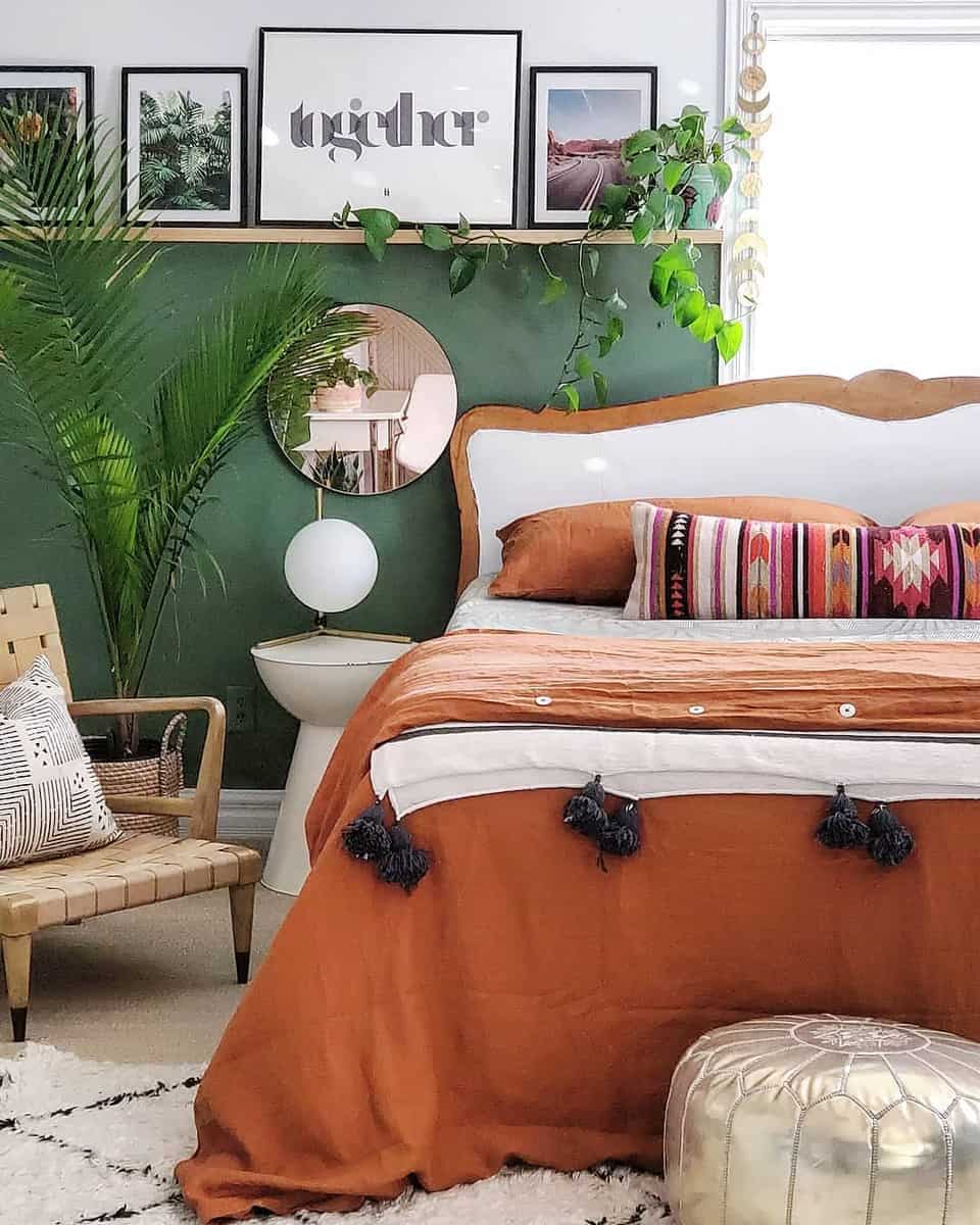 master-green-bedroom-ideas-blissfully_eclectic Cozy bedroom with green accent wall, wooden bed, orange bedding, patterned pillows, and leafy plants