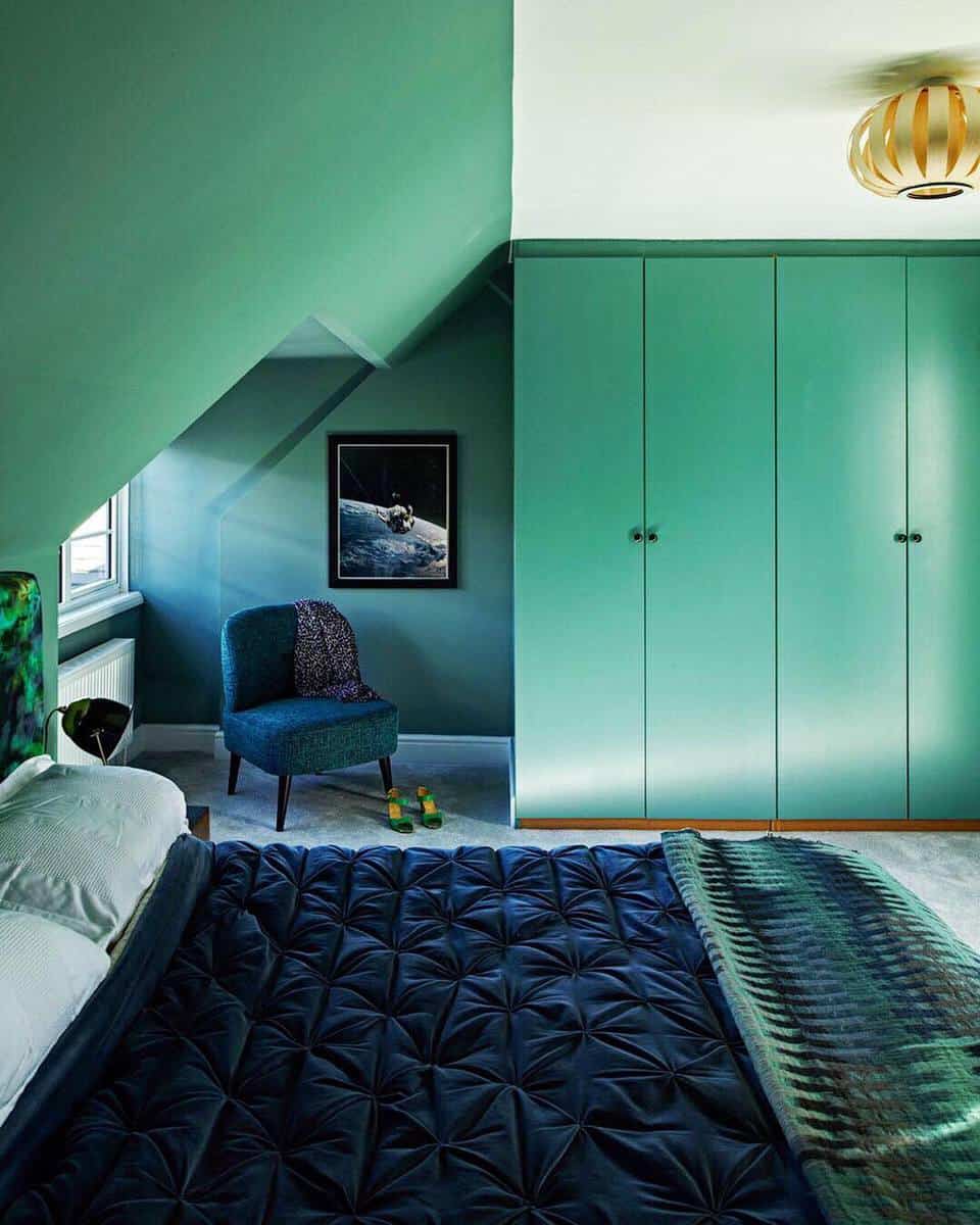 modern-green-bedroom-ideas-katelovejoyinteriors Green-themed bedroom with a large wardrobe, upholstered chair, and bed with dark bedding under sloped ceiling