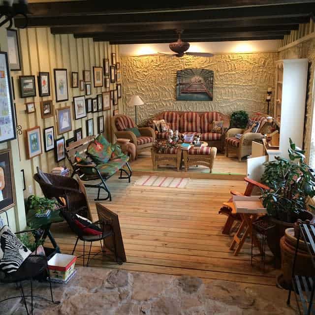 rustic-enclosed-patio-ideas-mustardseedmove wood deck rustic patio exposed roof beams framed wall art bookshelf wicker furniture