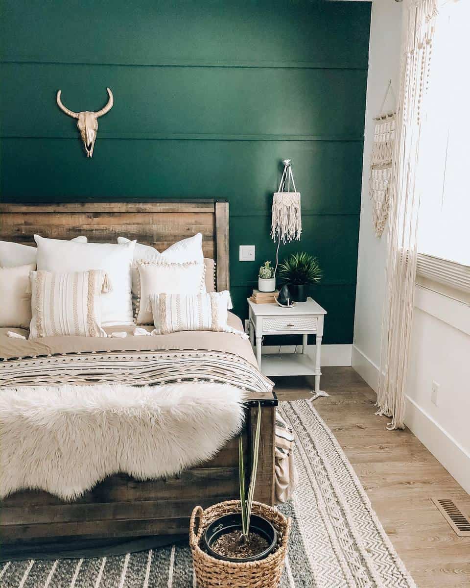 rustic-green-bedroom-ideas-smalltownstyleme Cozy bedroom with green accent wall, wooden bed, neutral bedding, and decorative wall art