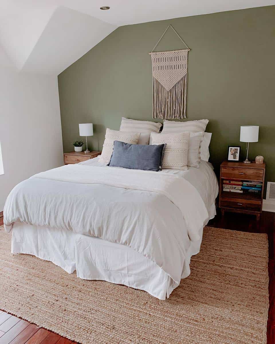 rustic-green-bedroom-ideas-thebeginnerhomie Cozy bedroom with a green accent wall, white bedding, pillows, wall hanging, bedside tables, and lamps