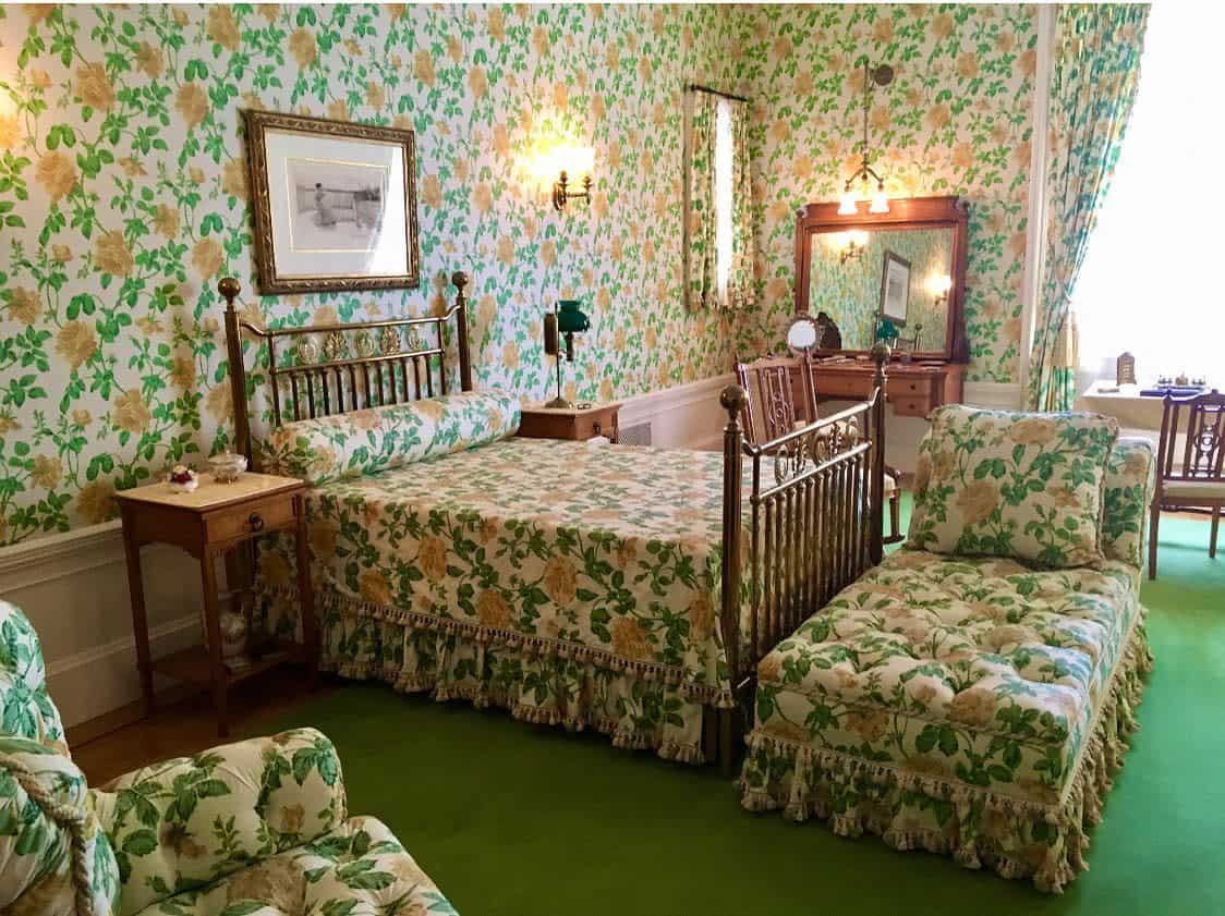wall-paper-green-bedroom-ideas-stephaniedavisb Vintage bedroom with floral wallpaper, matching bedspread and chaise, wooden furniture, and green carpet