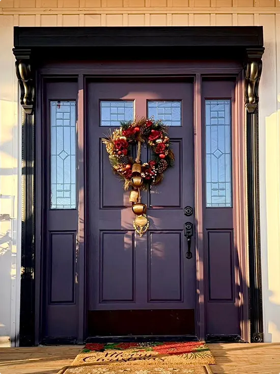 Eggplant-toned dark plum door and its wreath of red flowers, gold bells, and pinecones