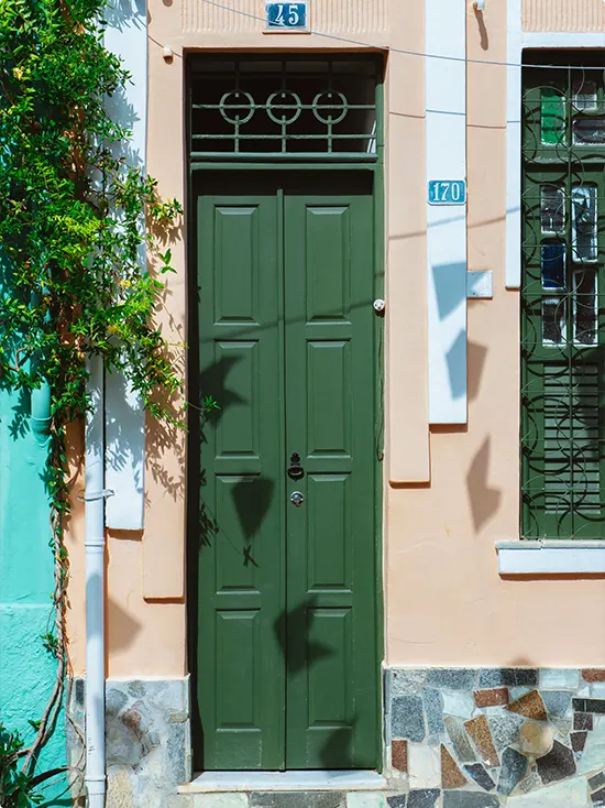 Forest Green Door on Peachy Pink Stucco House with Turquoise Pipe and Ivy at Side, Wrought Iron Above Door